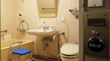 A small bathroom with a toilet, sink, and shower. There is a step stool next to the toilet and a handrail next to the sink.
