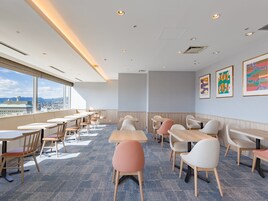 Un comedor moderno con mesas y sillas altas, ventanas amplias que ofrecen vistas a la ciudad y obras de arte en las paredes.