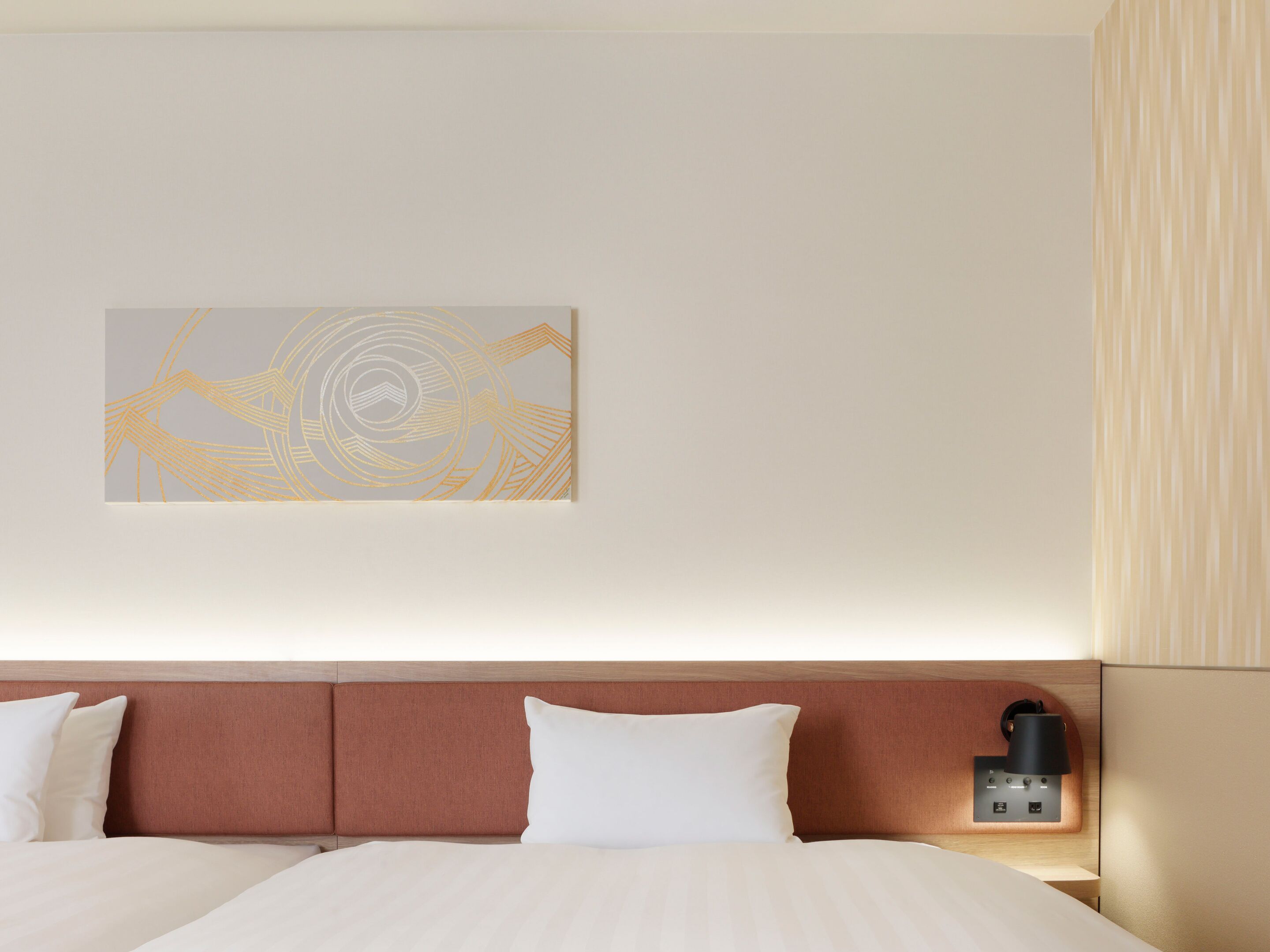 A hotel room with a bed, a headboard, a wall-mounted lamp, and a piece of wall art.