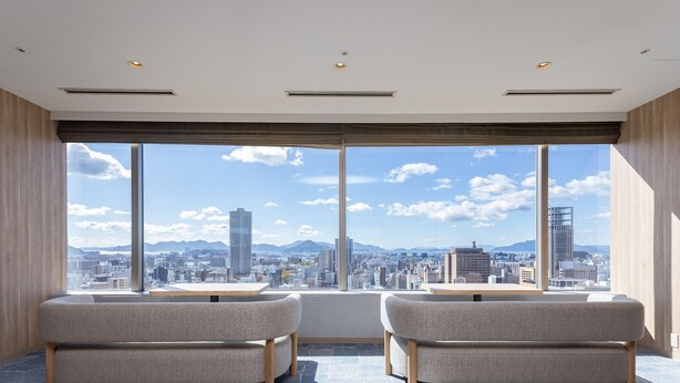 A modern hotel room with a large window offering a city view, two sofas, and a wooden table. - Mitsui Garden Hotel Hiroshima (Hiroshima)