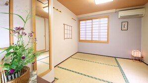 Een traditionele Japanse kamer met tatami vloeren, een shoji-scherm raam, een spiegel en een klein tafeltje met een plant in pot.