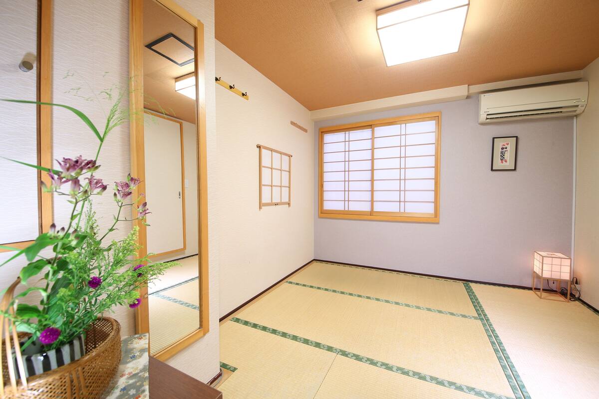 Ein traditioneller japanischer Raum mit Tatami-Boden, einem Shoji-Fenster, einem Spiegel und einem kleinen Tisch mit Blumentopf.
