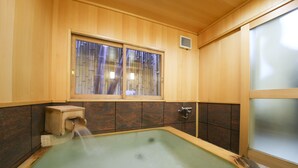 Een traditioneel Japans onsen met houten inrichting, een raam met bamboebladen en een kleine stenen structuur aan de rand van de warmwaterbron.