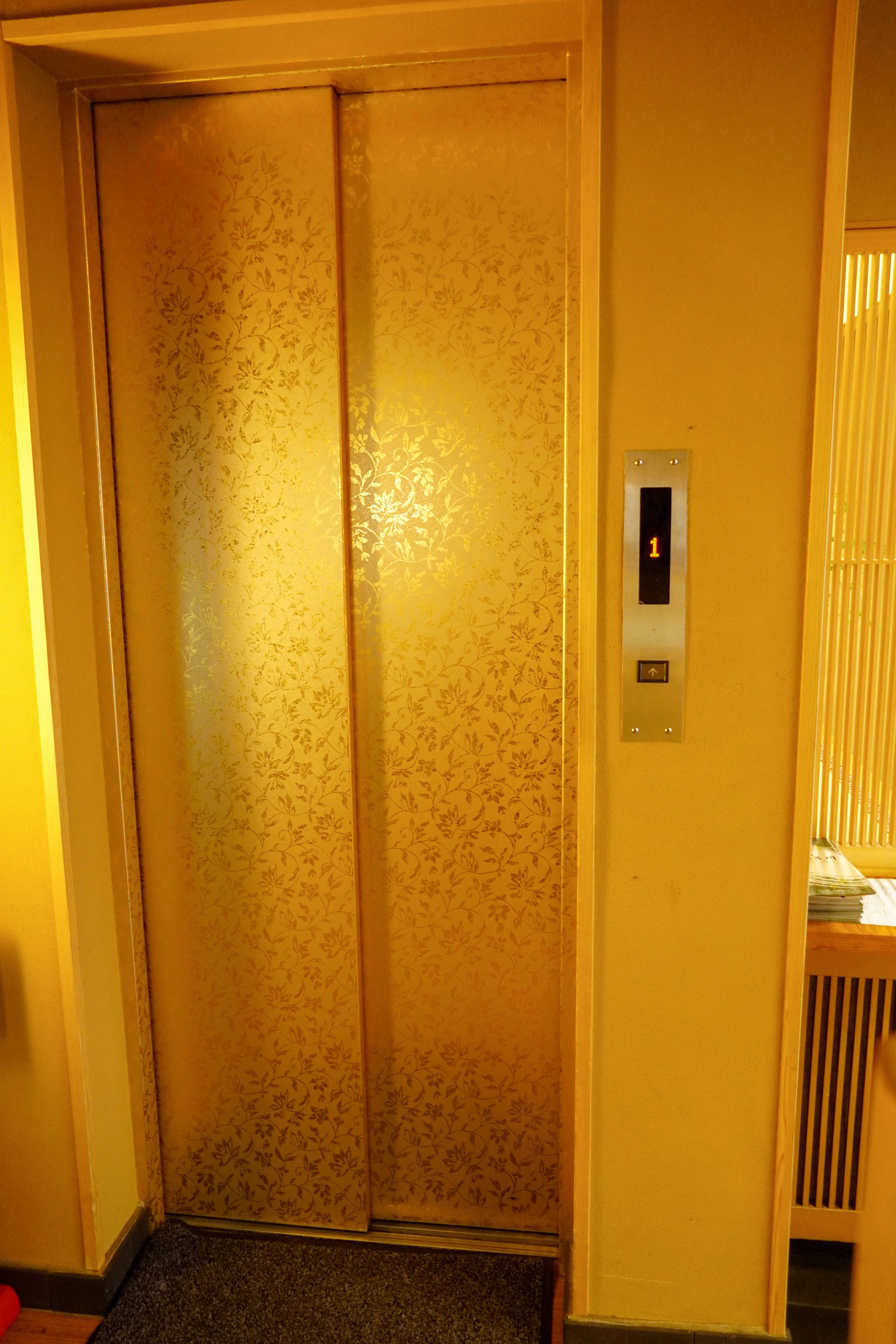 A closed elevator with floral wallpaper and a control panel with a button and a display showing the number 1.