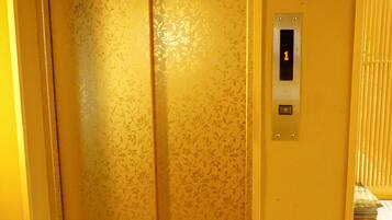 A closed elevator with floral wallpaper and a control panel with a button and a display showing the number 1.