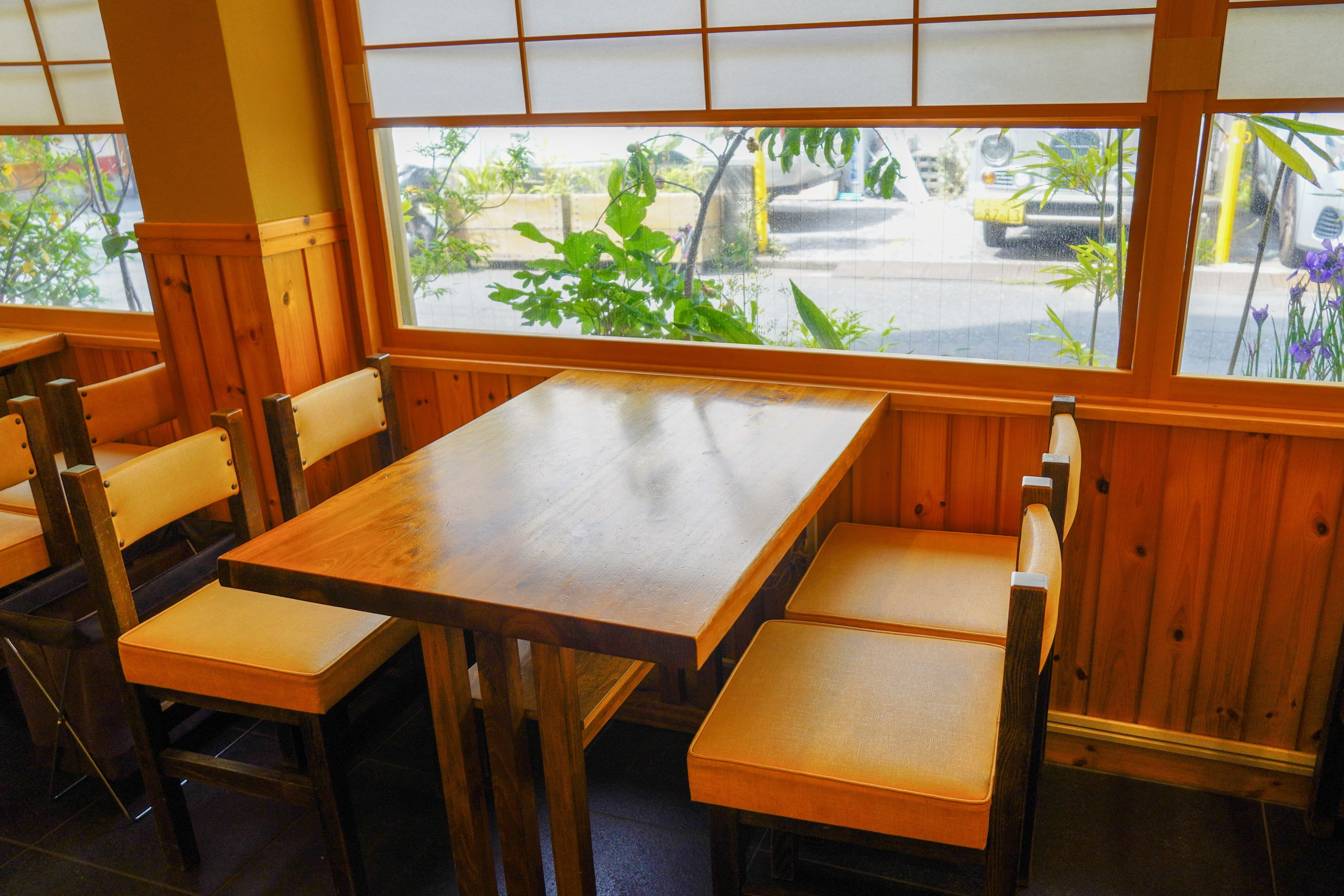 A restaurant with wooden tables and benches, large windows with a view of the street.