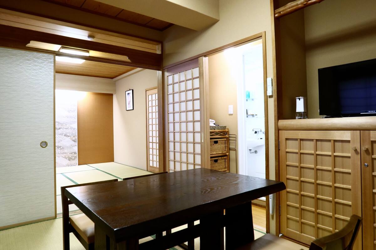 Ein traditioneller japanischer Raum mit Tatami-Boden, einem Holztisch und einem Fernseher auf einem Schrank.