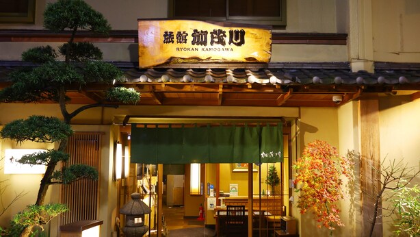 De entree van een traditioneel Japans restaurant, met een reclamebord, houten architectuur en potplanten.