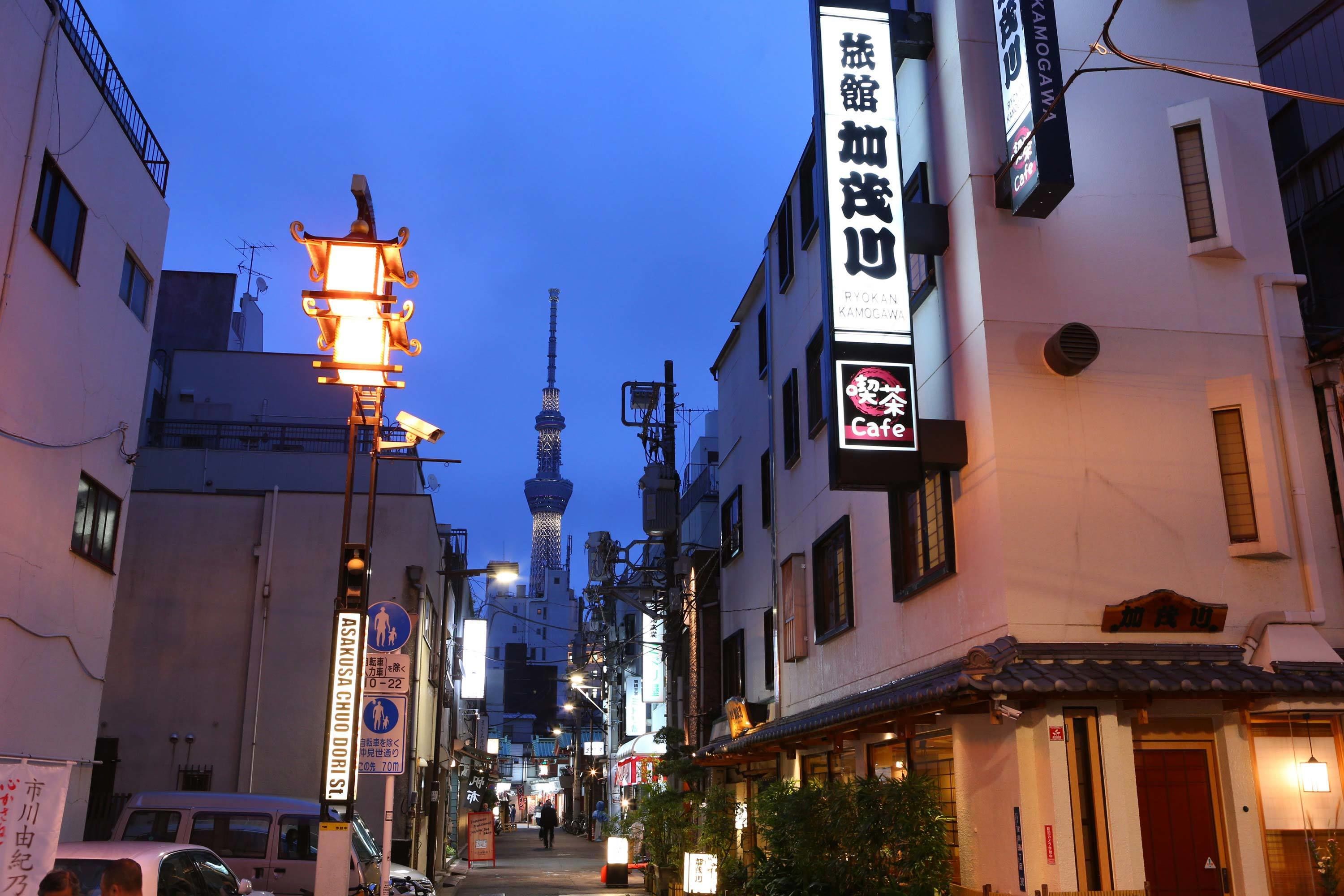 A narrow street with traditional Japanese architecture, including a lantern and signage for a cafe.