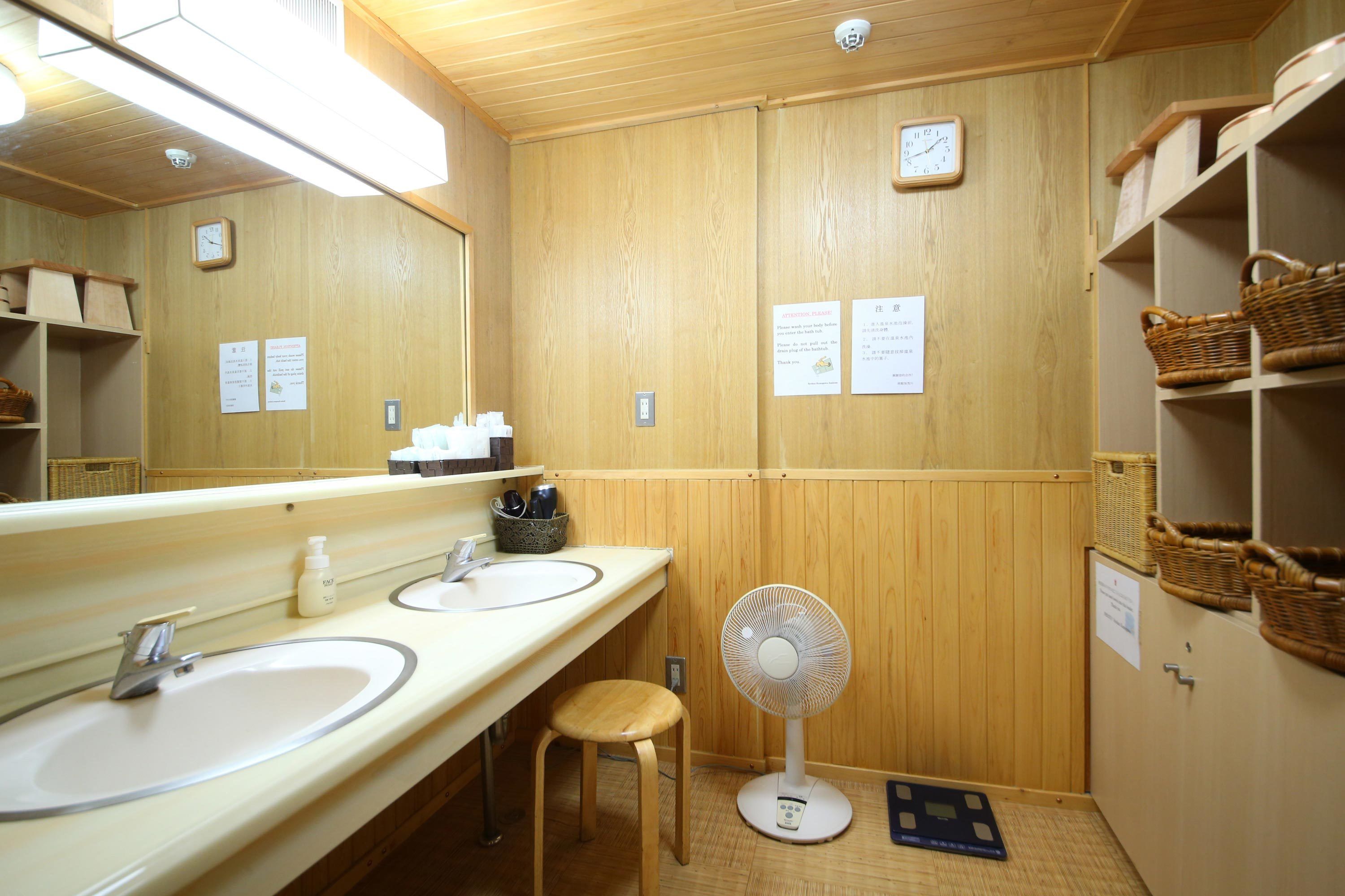 A wooden bathroom with two sinks, a mirror, a fan, and shelves with baskets.
