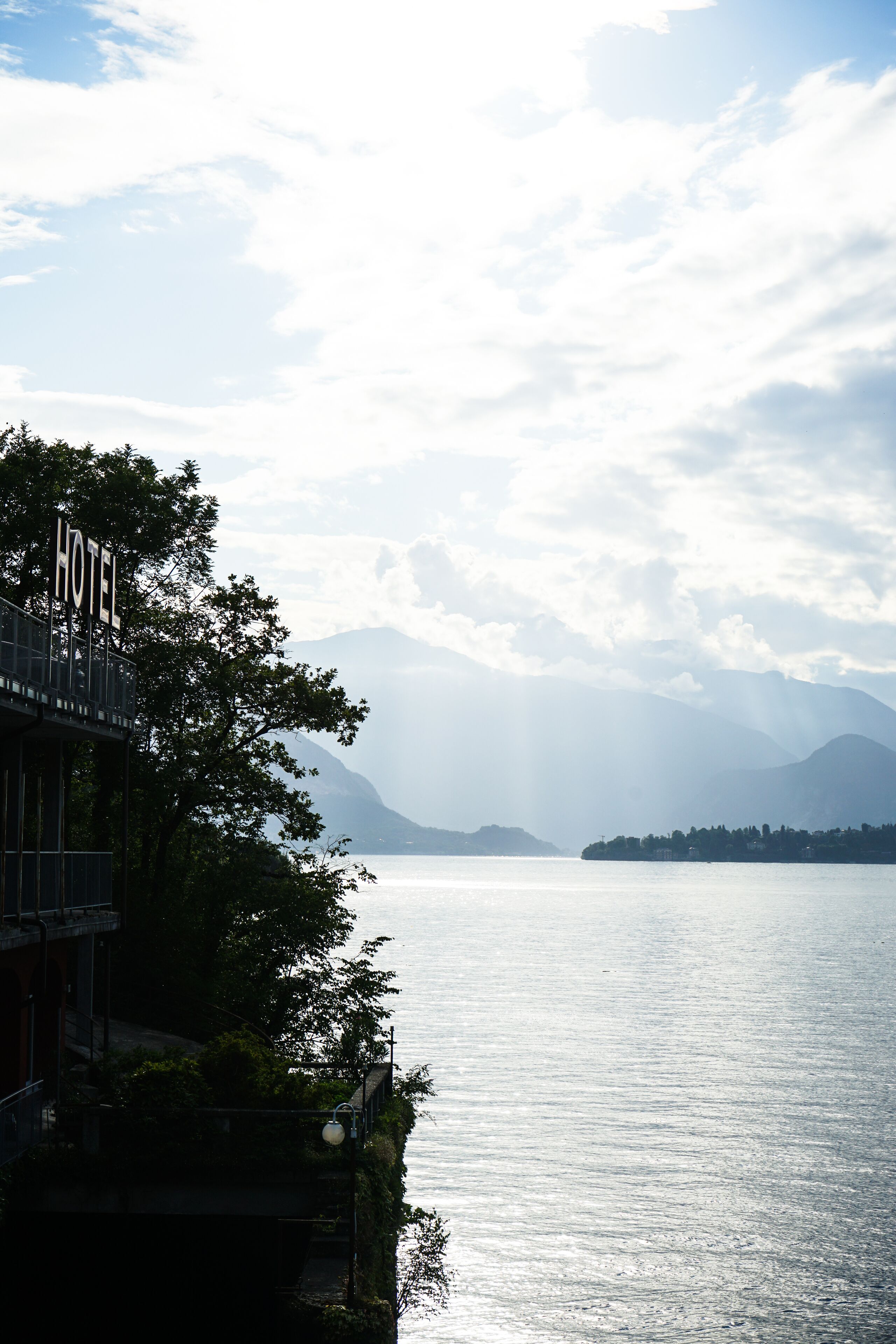Un hotel con un cartel, frente a un lago tranquilo y montañas a lo lejos.