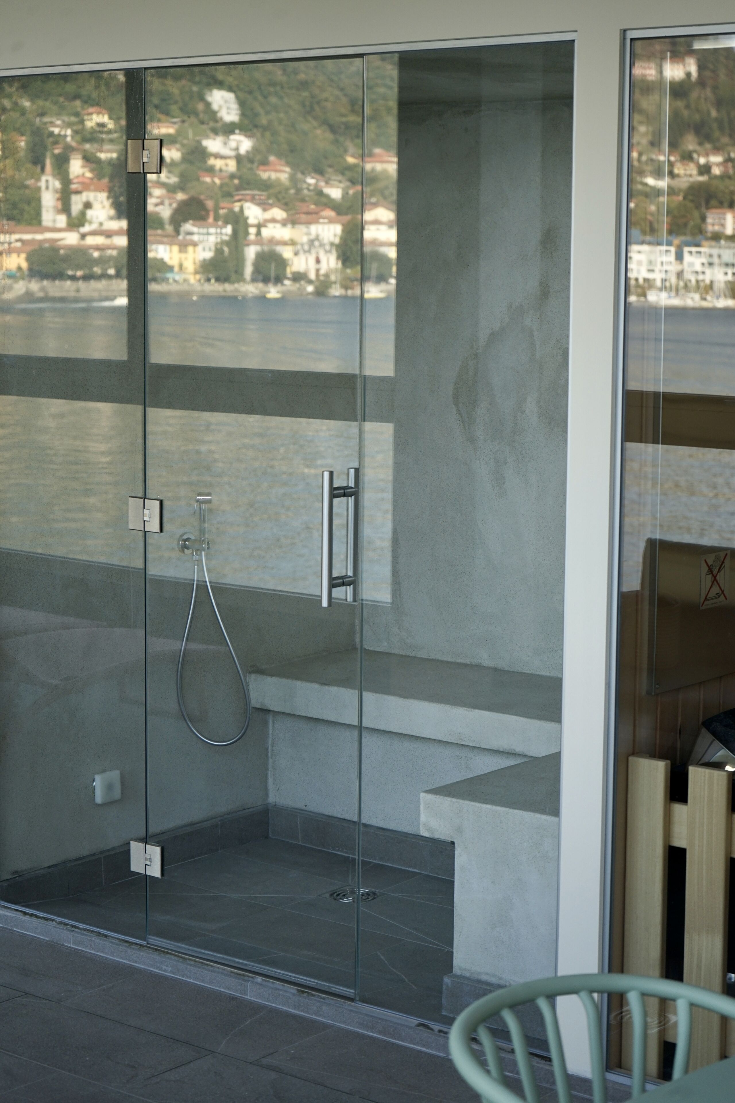 A glass-enclosed shower area with a view of a hillside town.
