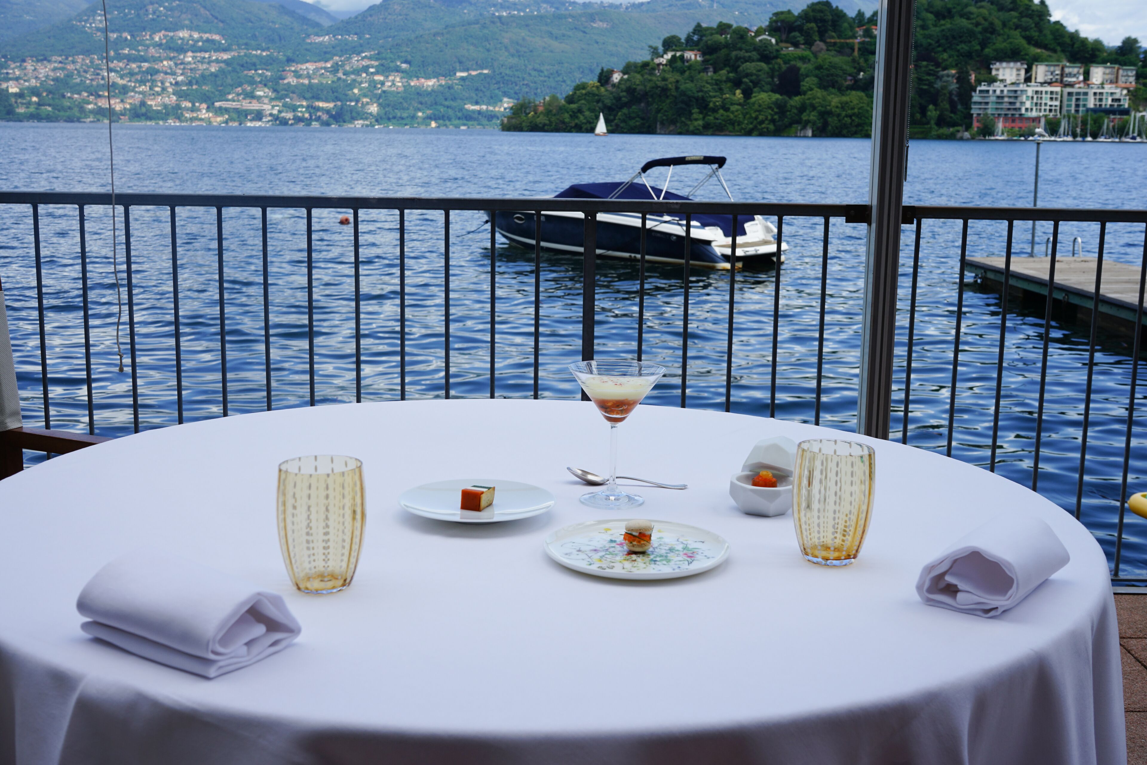 Mesa lista para comer con vista a un lago y un barco al fondo.