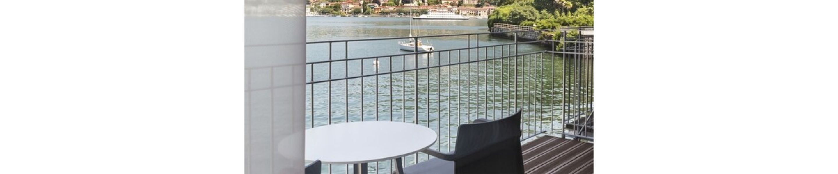 Un balcon avec une table et des chaises donnant sur une rivière paisible où se trouve un bateau.