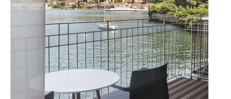 Un balcon avec une table et des chaises donnant sur une rivière paisible où se trouve un bateau.