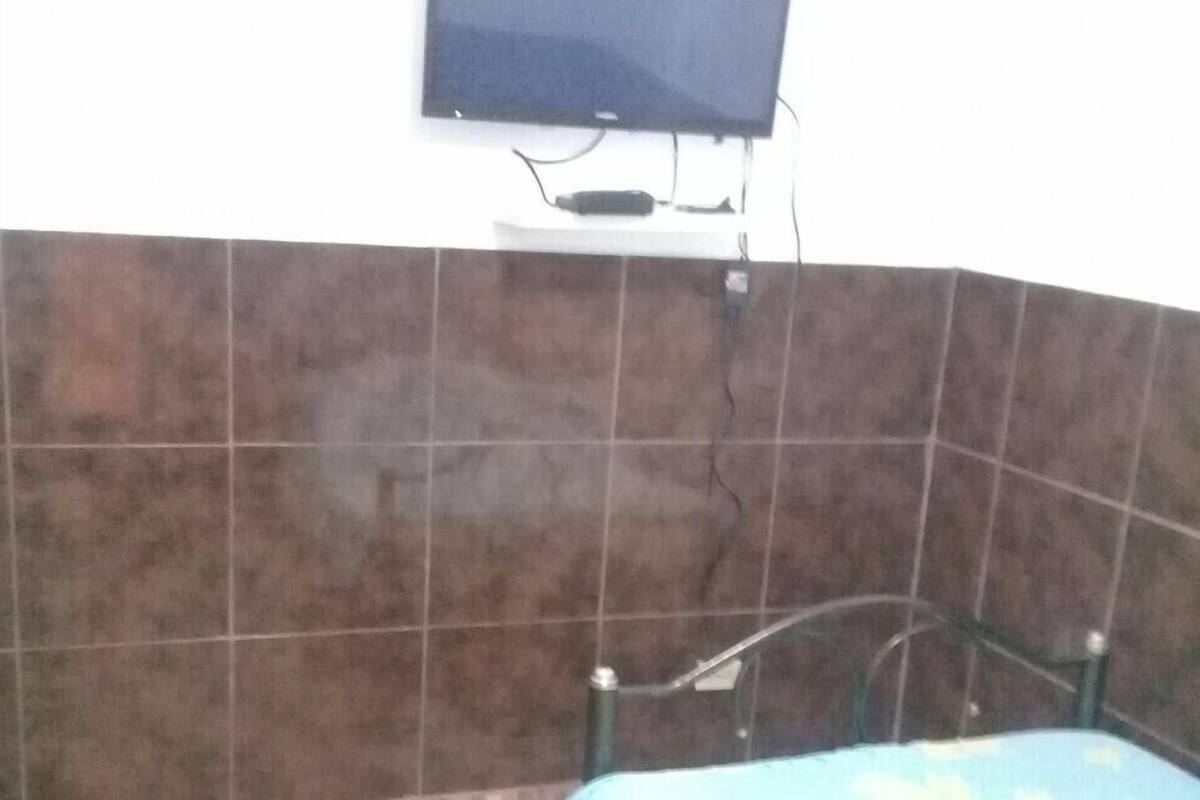 Una stanza con un letto, una televisione fissata al muro e pareti piastrellate.