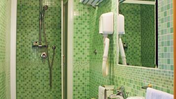 Ein Badezimmer mit grünen Mosaikfliesen, einer Dusche, einer Toilette und einem Waschbecken.