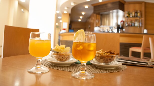 Une table avec deux verres contenant une boisson de couleur ambrée, un bol de noix et une assiette de nourriture.