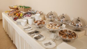 Une table de buffet proposant une variété de plats, notamment des pâtisseries, des fruits et des desserts, présentés sur des assiettes blanches et recouverts de couvercles en forme de dôme argenté.