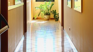 Un couloir d'hôtel avec un sol carrelé, une plante en pot et une fenêtre donnant sur l'extérieur.