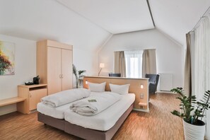 A modern hotel room with a large bed, a wooden desk, a chair, a potted plant, and a window with curtains. - Gut Gremmelin (Lalendorf)