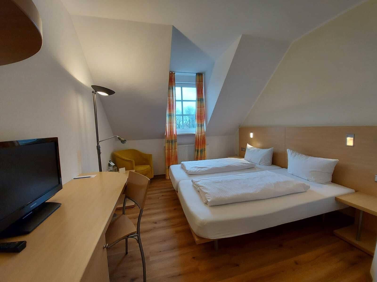 A modern hotel room with a large bed, a desk with a computer, a chair, and a TV.