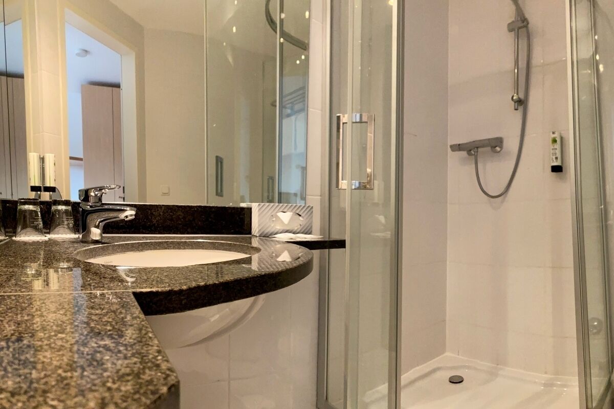 A modern bathroom with a granite countertop sink, a glass shower enclosure, and a large mirror.