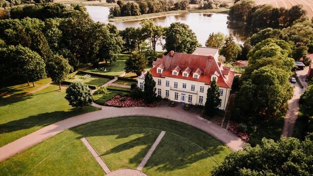 An aerial view of a large estate with a central circular lawn, a lake, and a building with a red roof. - Gut Gremmelin (Lalendorf)