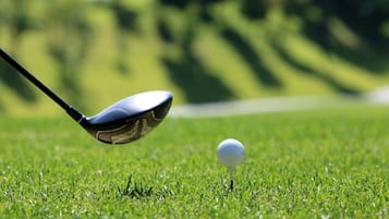 Um taco de golfe posicionado sobre uma bola de golfe num campo verde.