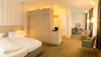 A hotel room with a large bed, a desk, a chair, and a wardrobe.
