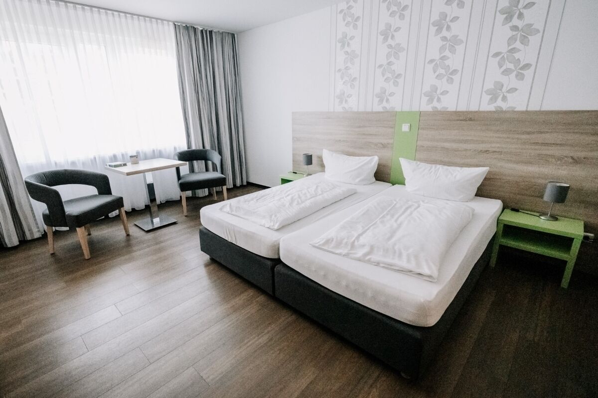 Een hotelkamer met een tweepersoonsbed, een bureau met stoel, een klein tafeltje en een nachtkastje in het groen.