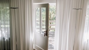 A room with a wooden floor, white curtains, and a door leading to an outdoor area with a wooden deck and trees. - Gut Gremmelin (Lalendorf)