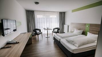 Une chambre d’hôtel avec deux lits, un bureau avec un téléphone, deux chaises, une télévision et une fenêtre avec des rideaux.