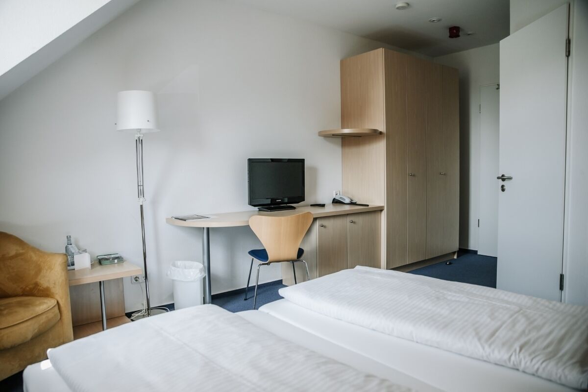 Habitación de hotel con dos camas, un escritorio con computadora, una silla, una lámpara y un armario.