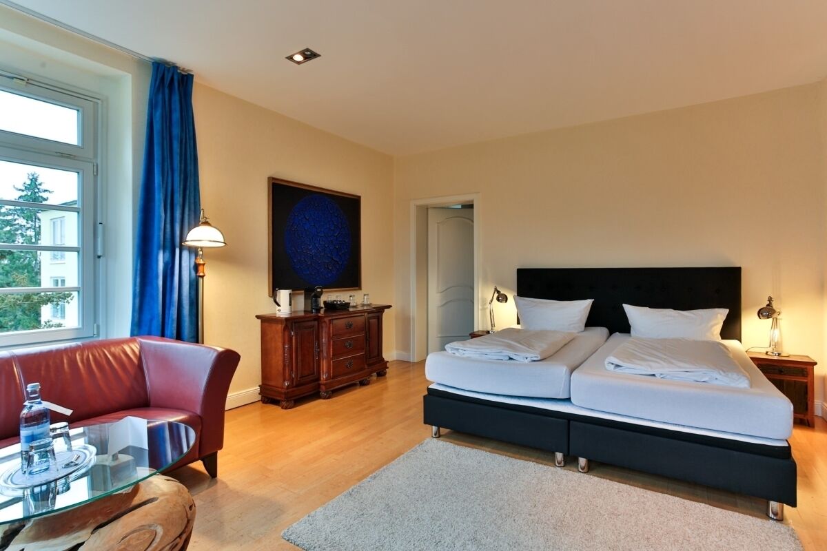 A hotel room with a bed, a sofa, a desk, and a window with curtains.