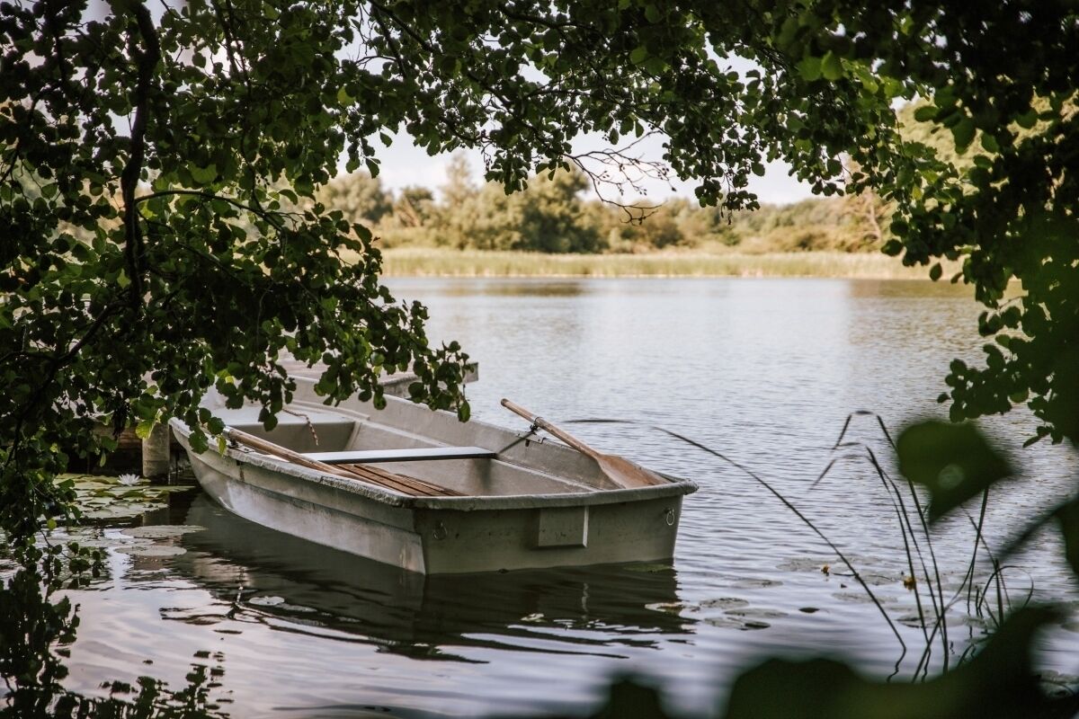 A small rowboat docked at a calm lake, surrounded by lush greenery.