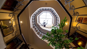 A grand staircase with a circular window at the top, surrounded by ornate metal railings and a plant in the foreground. - Encantada Casa Boutique Spa (Cusco)
