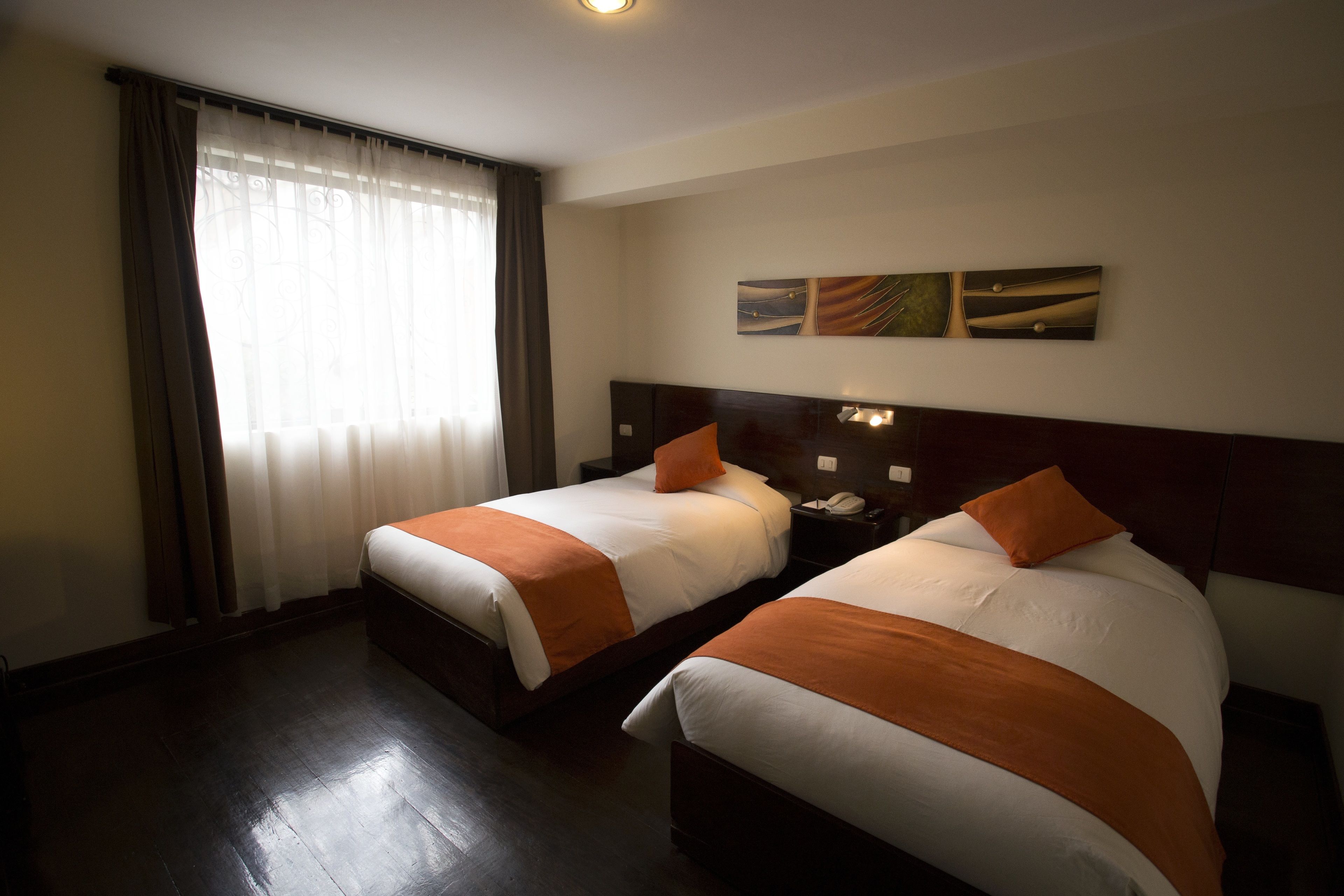 Habitación de hotel con dos camas, un ventanal con cortinas, una mesita de noche con teléfono y una obra de arte colgada en la pared.