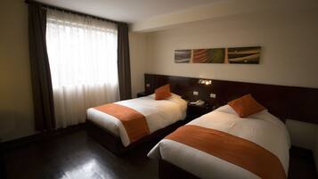 Habitación de hotel con dos camas, un ventanal con cortinas, una mesita de noche con teléfono y una obra de arte colgada en la pared.