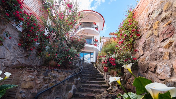 A stone staircase leading to a building with balconies, surrounded by flowering plants and a clear sky. - Encantada Casa Boutique Spa (Cusco)