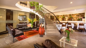 A spacious living area with a curved staircase, leather furniture, and a dining area with white tablecloths. - Encantada Casa Boutique Spa (Cusco)