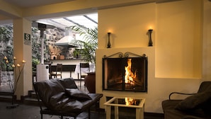 A cozy lounge area with leather sofas, a fireplace, and a view of a stone wall and plants. - Encantada Casa Boutique Spa (Cusco)