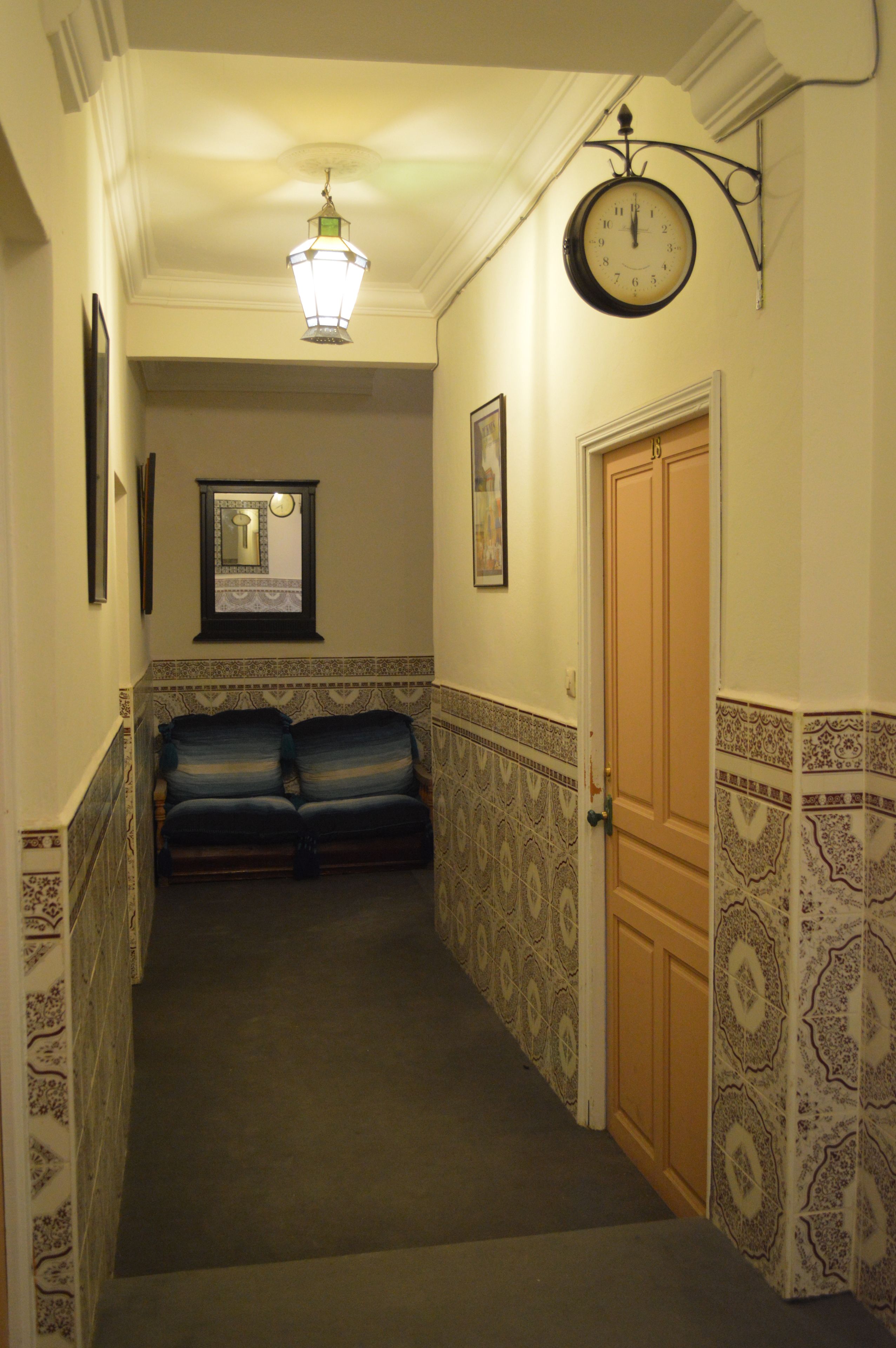 A hallway with patterned walls, a clock, a door, and a bench.