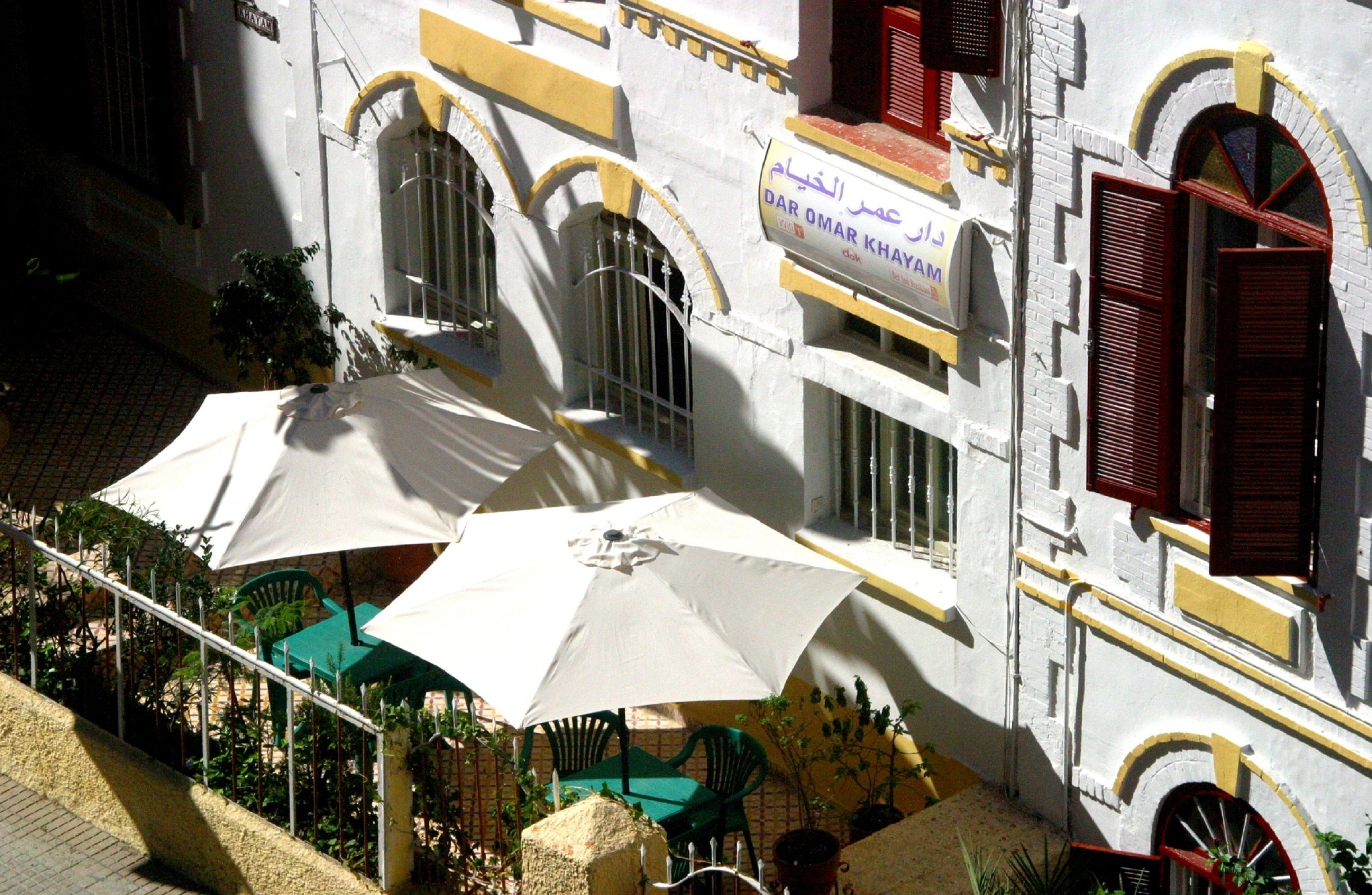 A building with a sign reading "DAR OMAR KHAYAM" and outdoor seating with umbrellas.