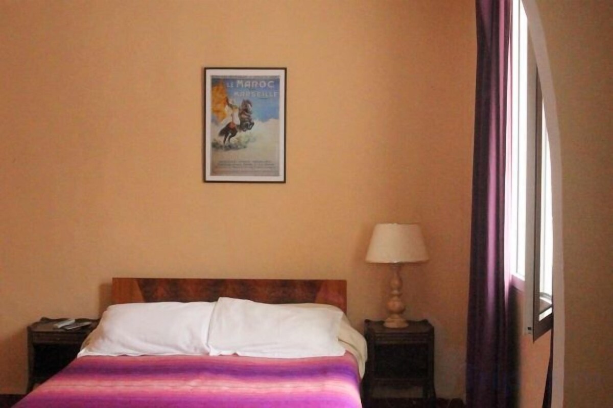 Una habitación de hotel con una cama, una mesita de noche, una lámpara y un cartel en la pared.