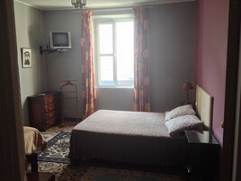 Un dormitorio con cama, cómoda, televisión y ventana con cortinas.