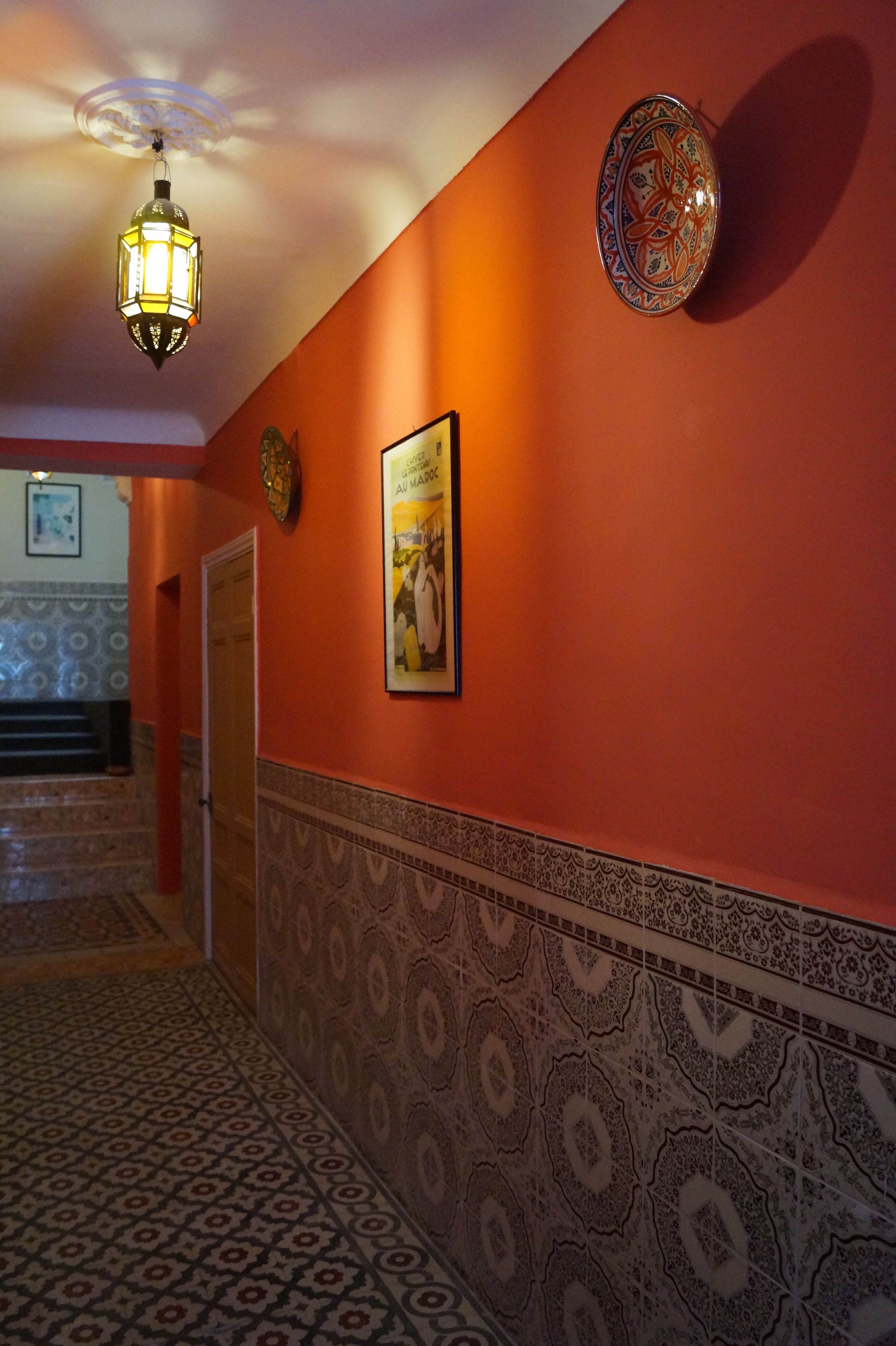 A hallway with patterned tiles, a decorative wall plate, and a framed poster.