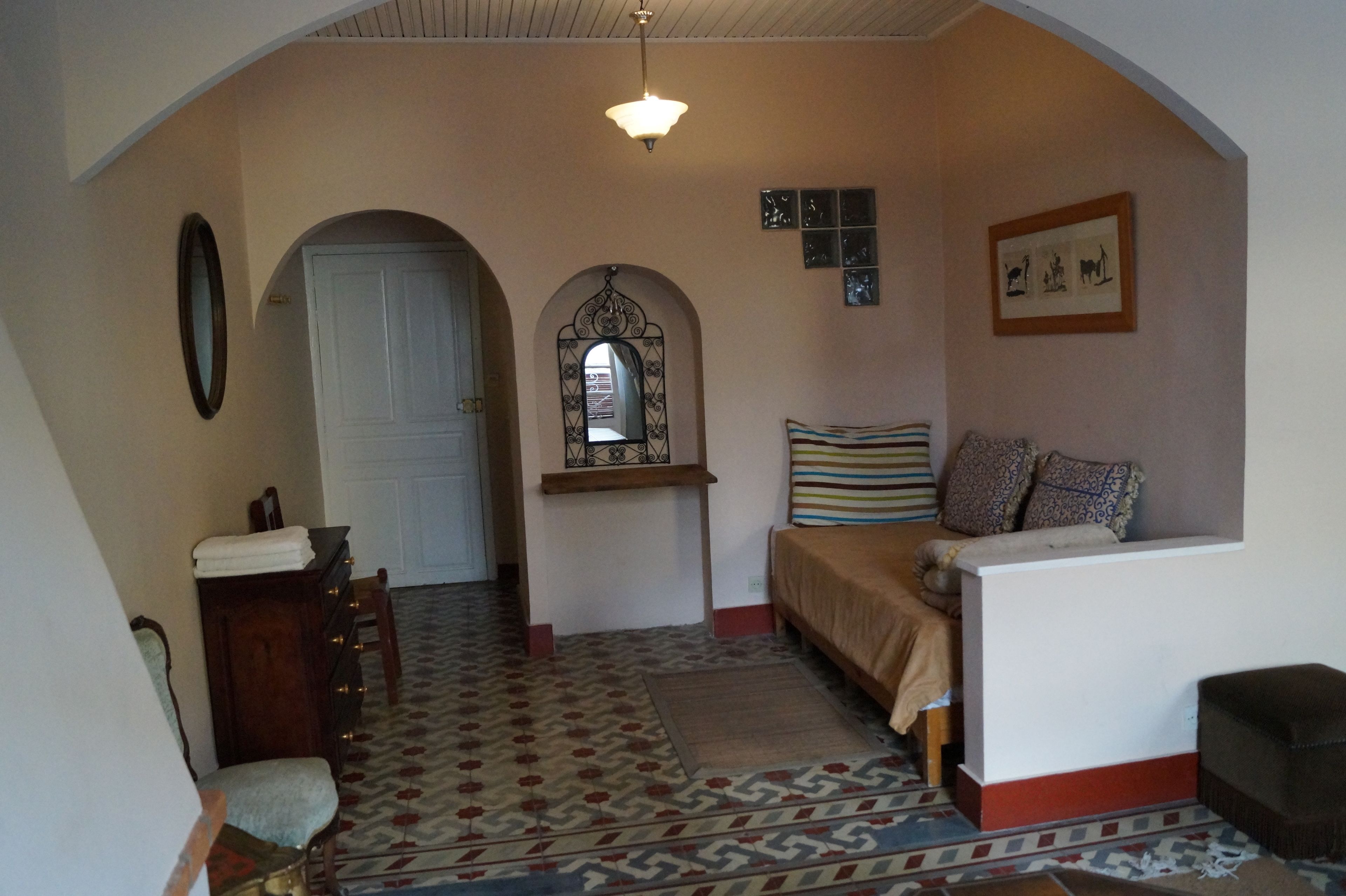 A room with a bed, a dresser, a mirror, and a window with a decorative arch.