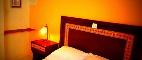 A hotel room with a bed, a nightstand with a lamp, a wall-mounted light fixture, and a framed picture on the wall.