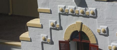 Un bâtiment à la façade blanche, doté d’une fenêtre centrale en arc surmontée de volets rouges et d’une tour ornementale coiffée d’un toit en forme de flèche.
